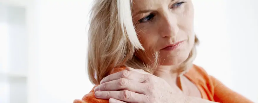 Mature blonde woman wearing orange touching her aching shoulder