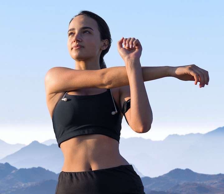 Healthy young woman stretching her arms with blue mountains in the background