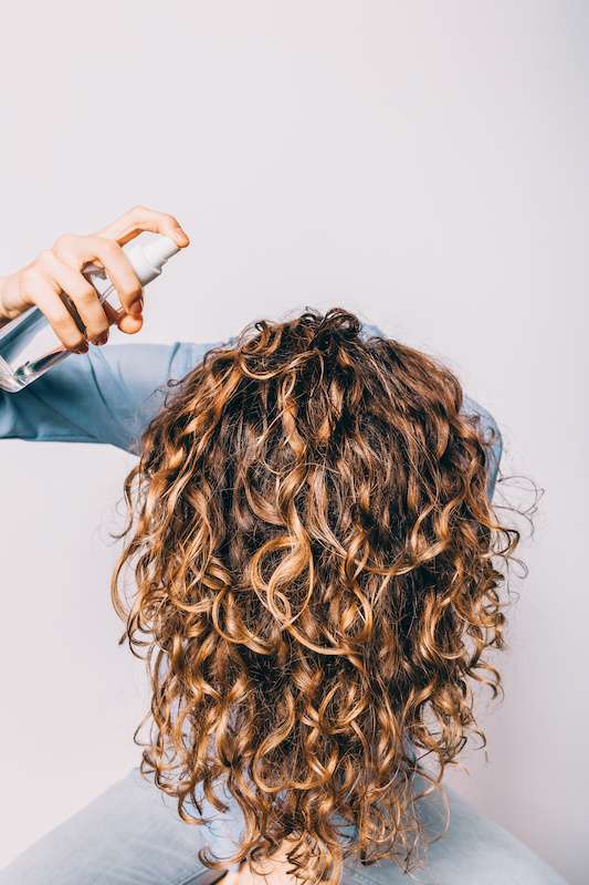 woman spraying hair product into hair