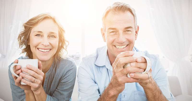 Smiling middle aged couple sitting on the couch having coffee