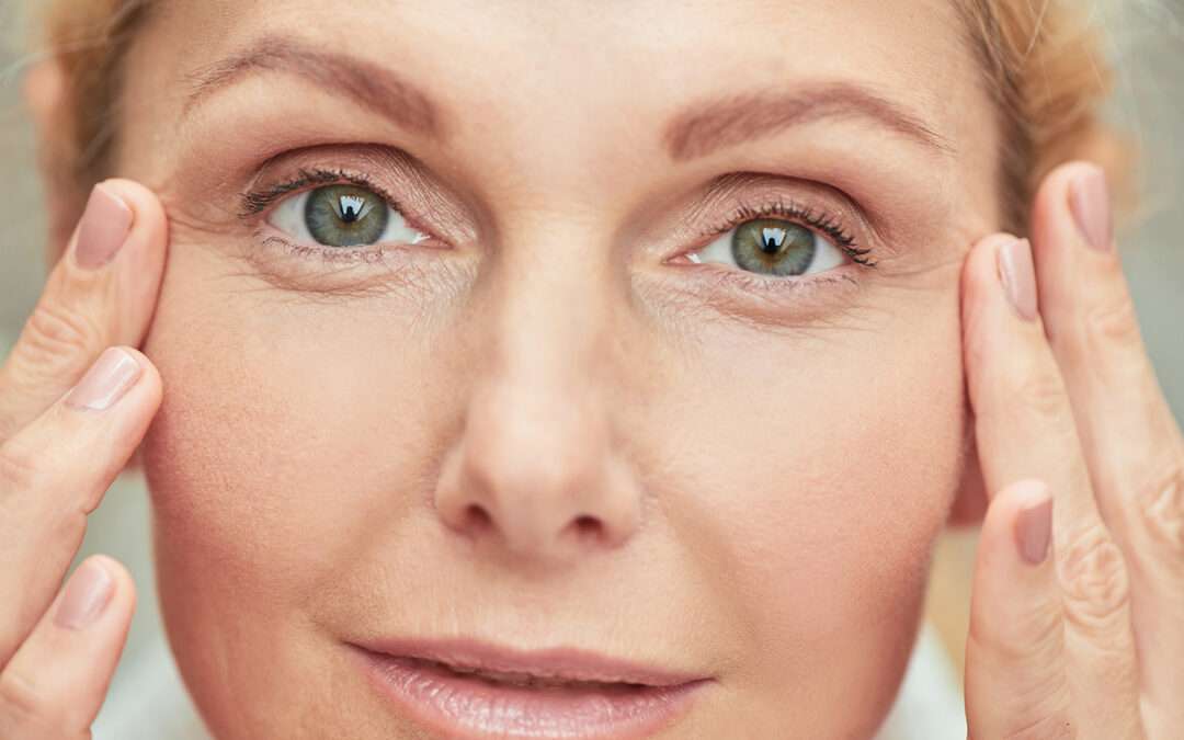 Woman with fingers near green eyes looking at camera