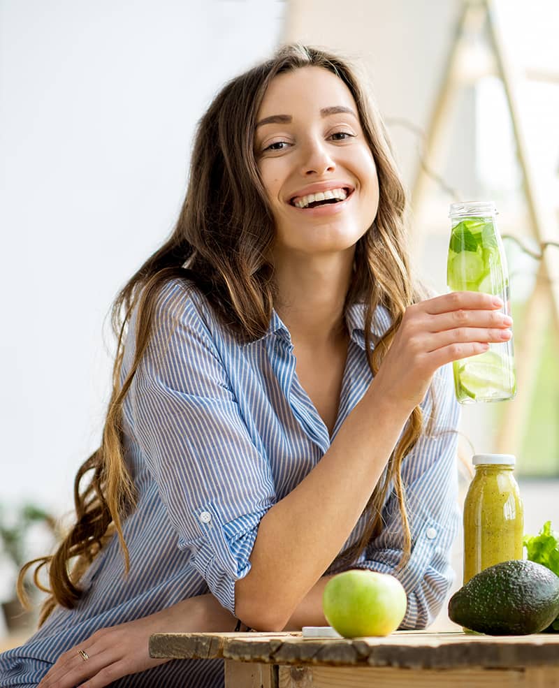 A woman smiles as she holds a bottle of infused water.
