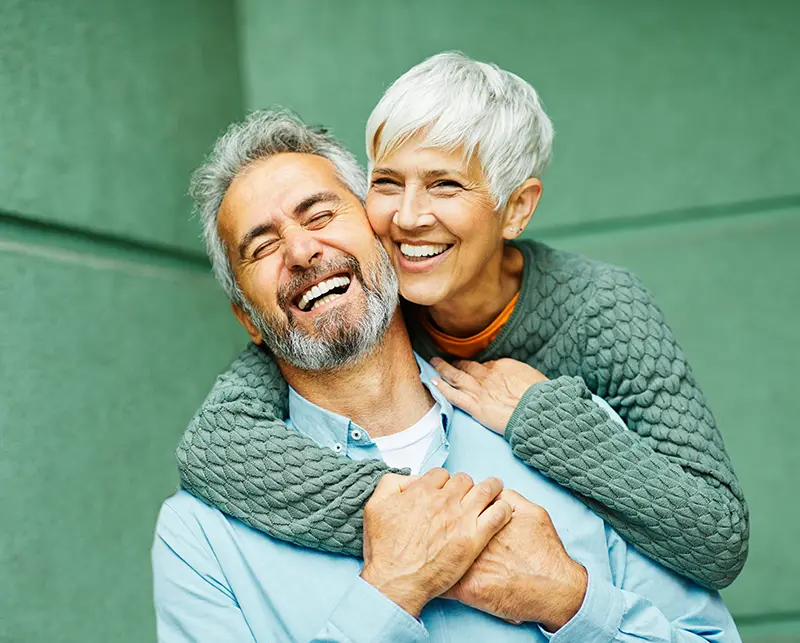 A couple smiles at the camera as they hug.